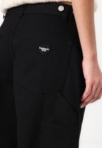 Sorte cargo bukser med et hjerteformet broderet patch med "Carhartt WIP" logo. Lavet af holdbart stof med synlige syninger.