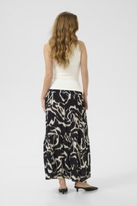 Falda maxi con un patrón abstracto en blanco y negro, diseño plisado y tela fluida. Combinada con una camiseta blanca ajustada y zapatos de slide negros.