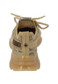 Chaussure de sport beige avec une tige en tricot texturé, semelle en caoutchouc brillant et accents décoratifs, y compris une étiquette métallique et des lacets.