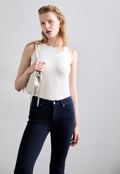 Top sans manches blanc au toucher lisse, associé à un jean slim noir avec fermeture à boutons et poches avant discrètes.