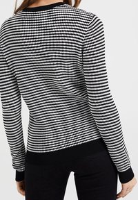 Maglione a motivo bianco e nero con motivo a diamante texturizzato, maniche lunghe e orlo nero solido. Attillato con scollo rotondo.