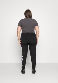 Svarta leggings har en vit logotyptryck längs sidan, tillsammans med en åtsittande grå t-shirt med kort ärm, bärs med svarta ankelstövlar.