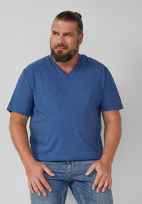 Niebieska koszulka z krótkim rękawem i dekoltem w serek, wykonana z teksturowanej tkaniny, w zestawie z jasnymi dżinsami. Koszulka ma luźny krój i subtelny wzór.