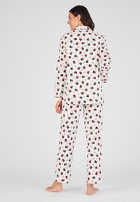 Set di pigiama da donna in tessuto bianco con un motivo di regali e fiocchi di neve. Include una camicia con bottoni e pantaloni larghi, con maniche lunghe.