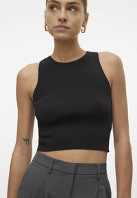Top corto negro con relieve, cuello redondo y diseño sin mangas, combinado con pantalones grises de talle alto. Textura suave, detalles mínimos.