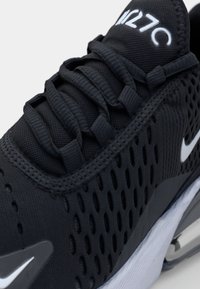 Fekete sportcipő, textúrált hálós felsőrésszel, látható perforációkkal és fehér swoosh logóval, párnázott talppal a kényelem érdekében.