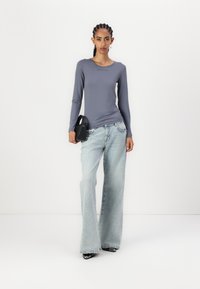 Long-sleeve light gray top with "BLANCHE" text, paired with light blue wide-leg denim jeans and a small black handbag. Slim fit, smooth texture.