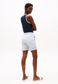 Tricou fără mâneci de culoare bleumarin cu margine albă, pantaloni scurți de un bleu deschis cu tiv răsucit și sandale bej. Material neted și design simplu.