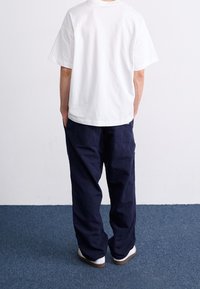 Bílé bavlněné tričko, volný střih, krátké rukávy, spojené s námořnicky modrými cargo kalhotami, dvě zadní kapsy, nošeno s bílými botami.