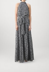 Maxikleid mit Neckholder-Ausschnitt, schwarzem Stoff mit unregelmäßigen weißen Polka-Punkten, gebundenem Taillengürtel und einem fließenden, gemusterten Rock.