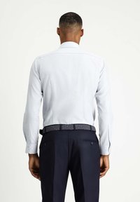 Camicia a maniche lunghe azzurro chiaro con tessuto testurizzato, colletto stretto e polsini con bottoni, abbinata a pantaloni blu scuro e una cintura a fantasia.