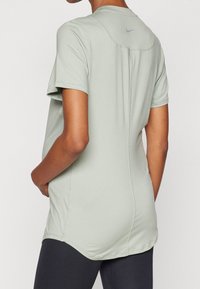 Camiseta deportiva verde claro de manga corta, con un dobladillo curvado y un detalle en la costura posterior. Presenta un pequeño logo gris de Nike en el cuello de la parte posterior.