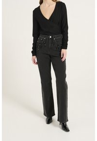 Schwarzes Langarm-Wickeltop mit tiefem V-Ausschnitt und taillierten Ärmeln, kombiniert mit hochgetriebenen schwarzen Jeans mit Perlenverzierungen.