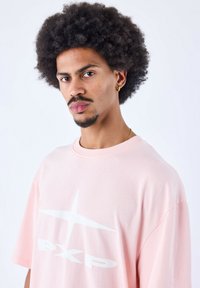 Camiseta de algodón rosa claro con una gran impresión gráfica blanca y un corte relajado. Mangas cortas y escote redondo.