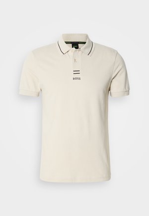 Rövid ujjú, bézs színű, pamutból készült pólóing, klasszikus gallérral, két gombbal, és fekete logóval, alatta két fekete csíkkal.