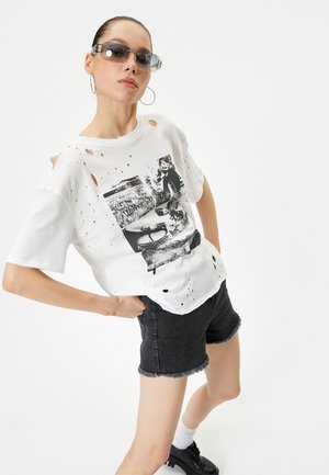 Hvid distressed T-shirt med grafisk print, parret med sorte denimshorts med frynsede kanter. Accessories inkluderer solbriller og hoops øreringe.
