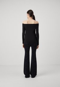 Zwarte off-shoulder lange mouwen top gecombineerd met uitlopende donkerblauwe geblokte broek. De stof lijkt glad; de broek heeft een subtiel geometrisch ontwerp.