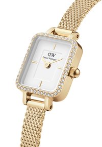 Gold-tone rectangular watch with a crystal-studded bezel, white dial, gold hands, and a fine mesh strap. Brand name "Daniel Wellington" displayed.
