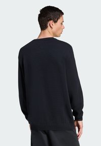Sweater preto de malha com gola redonda e punhos canelados, apresentando um ajuste descontraído e um tecido texturizado, visto de costas.