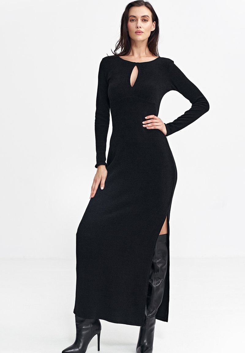 Czarna sukienka o długim rękawie z dekoltem w kształcie łezki i bocznym rozcięciem, uszyta z prążkowanej tkaniny. Stylizowana z wysokimi czarnymi botkami.