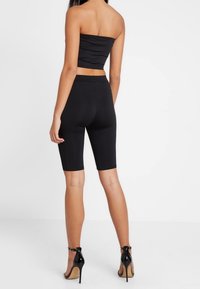 Svart strapless-top kombinerad med högmidjade svarta cykelshorts. Modellen bär svarta stilettklackar. Slät tyg med en åtsittande design.