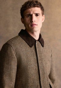 Brown checkered jacket with a dark brown corduroy collar, featuring a button closure and a textured fabric. No visible patterns or accents.