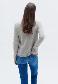 Maglione grigio lavorato a maglia con scollatura rotonda, maniche lunghe e dettagli con bottoni sui polsini, abbinato a jeans in denim blu, visto da dietro.