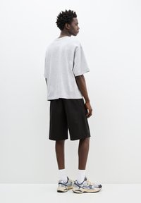 Tricou oversize gri cu mâneci scurte, asortat cu pantaloni scurți negri. Purtați cu sosete albe și adidași cu model, văzuți din spate.