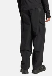 Black cargo pants with a relaxed fit, featuring side pockets and a textured fabric, paired with black footwear. Simple, functional design.