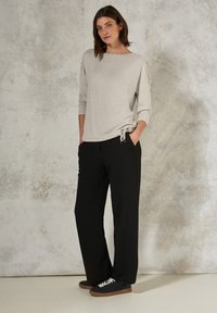 Maglietta grigia chiara a maniche lunghe con dettaglio arricciato sulle spalle, abbinata a pantaloni neri a gamba larga e sneaker scure con lacci bianchi.