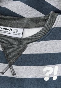 Sudadera de rayas en colores gris y azul marino, con un cuello acanalado, una pieza triangular única y un detalle impreso en blanco con "?!".