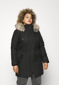 Parka noire avec une capuche en fourrure, deux poches avant et une taille élastique. Texture lisse et design mi-long pour la chaleur et la couverture.