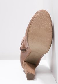 Bottine en cuir marron avec une finition texturée, un talon effilé et des coutures décoratives. Les semelles présentent un motif floral en relief.