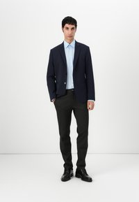 Blazer navy sobre una camisa de botones azul claro, combinado con pantalones gris oscuro y zapatos negros. Tejidos suaves con un ajuste a medida y detalles en la solapa.