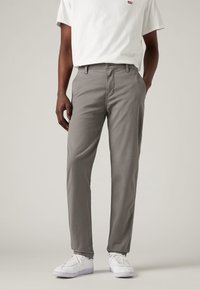 Chinos en coton gris avec une coupe droite, dotés de passants pour ceinture, de poches avant et d'une fermeture à bouton, associés à des baskets blanches.