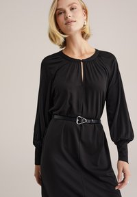 Fekete ruha hosszú ujjakkal, ráncolt vállakkal, kulcslyuk nyakkivágással és fekete övvel, ezüst szív alakú csattal. Sima textúra.