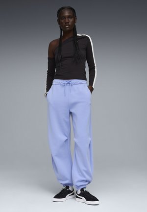 Sort langærmet top med asymmetrisk skulder og hvid stribe, kombineret med lyse lilla joggingbukser og sorte sneakers.