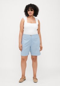 Top de tirantes blanco con escote cuadrado, combinado con pantalones cortos azules claros hasta la rodilla, con dobladillo enrollado y cierre de botón. Zapatos planos color topo y gafas de sol.