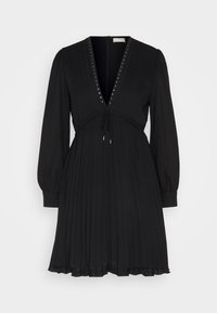 Vestito nero con scollatura a V profonda e gonna plissettata. Dettagli includono borchie metalliche lungo la scollatura e vita con cordoncino. Maniche lunghe.