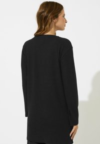 Schwarzer Langarmpullover mit lockerer Passform, runden Halsausschnitt und seitlichen Schlitzen für eine einfache Beweglichkeit, aus weichem Strickstoff gefertigt.