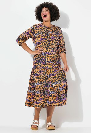 Abito con stampa leopardata in arancione, nero, viola e bianco. Maniche lunghe a sbuffo, scollo rotondo e gonna a strati. Indossato con sandali bianchi.