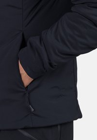 Sort pufferjakke stof med en sidelomme og lynlås. Glat tekstur med et tætsiddende ærmedesign.