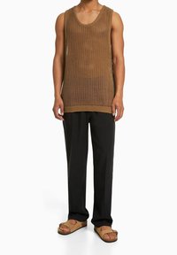 Brown knitted tank top with a loose fit and large armholes, paired with black tailored trousers and light brown sandals.