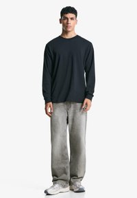 Black long-sleeve shirt paired with light gray straight-leg jeans and gray sneakers. The shirt has a round neck and ribbed cuffs.