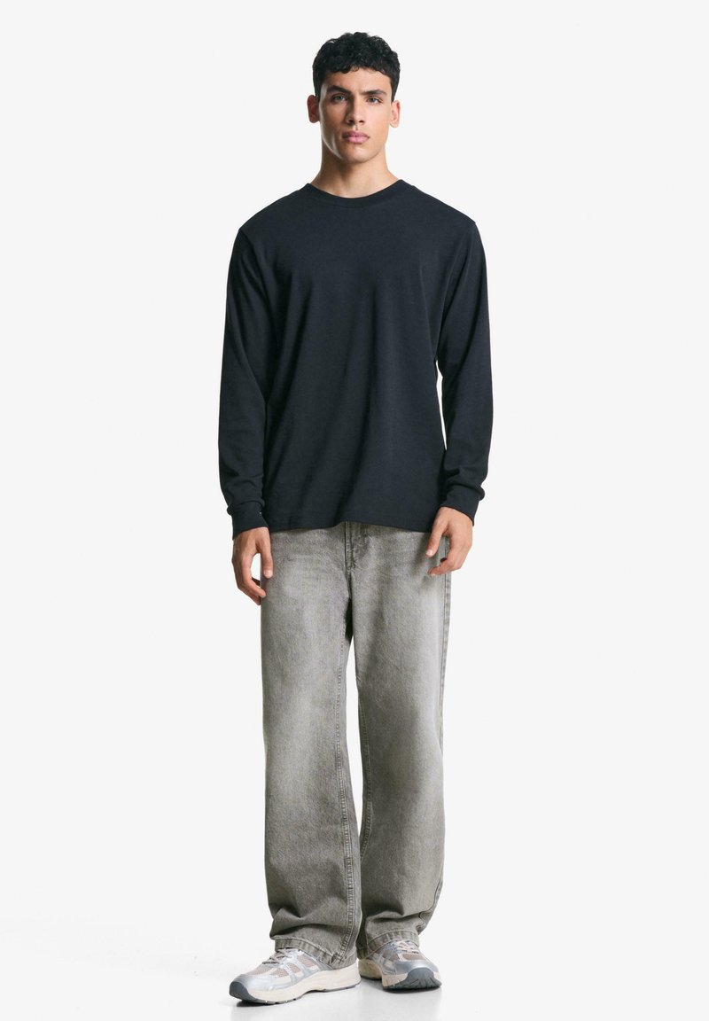 Black long-sleeve shirt paired with light gray straight-leg jeans and gray sneakers. The shirt has a round neck and ribbed cuffs.