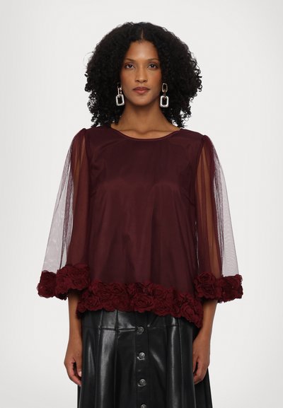 Top bordeaux cu mâneci lungi transparente, broderie florală la tiv și decolteu rotund. Asortat cu o fustă din piele neagră.