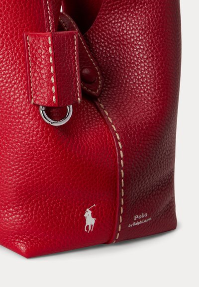 Červený kožený roh tašky s textúrou, bielym logom Polo, béžovým prešitím a strieborným kovovým krúžkom na popruhu.