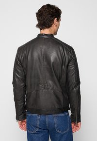 Giacca in pelle nera con texture a coste lungo le spalle e i lati, dotata di chiusura con zip e design aderente.