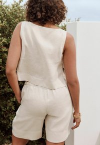 Haut sans manches beige clair associé à un short assorti, fabriqué dans un tissu texturé. Accentué par une coupe décontractée et des détails de design subtils.
