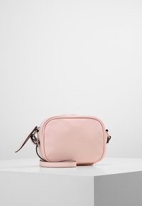 Piccola borsa a tracolla rettangolare in pelle rosa chiaro con bordi arrotondati e tracolla removibile su superficie bianca.